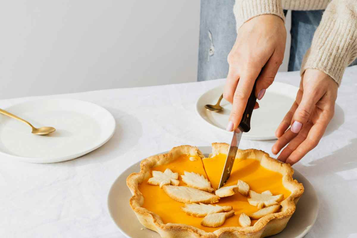 una mano taglia la torta alla zucca con un coltello