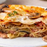 Una porzione di lasagne con funghi porcini e salsiccia in un piatto