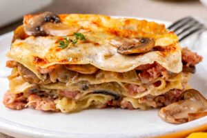 Una porzione di lasagne con funghi porcini e salsiccia in un piatto