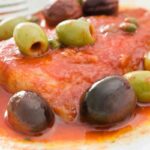 primo piano di una fetta di pesce spada alla livornese con olive e capperi e sugo di pomodoro